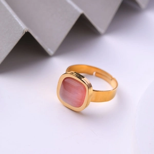 Gros plan d'une bague ajustable dorée ornée d'une pierre précieuse rose carrée sur fond blanc