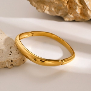 Dettaglio del bracciale quadrato in oro lucido su pietra con luce calda di lusso