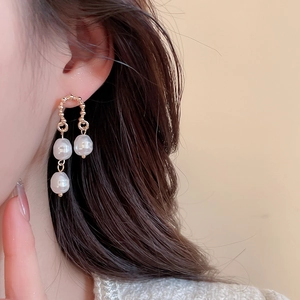 Close-up of elegant gold drop earrings with white pearls and layered tassel design