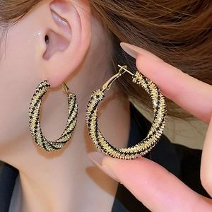 Macro detail of luxury black and gold twisted hoop earrings worn by a model