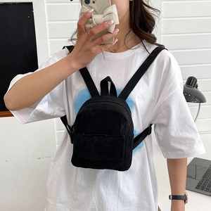 Detail of a black corduroy mini backpack worn as a chest bag in a bright interior setting