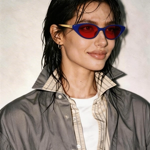 Close-up of model wearing blue cat-eye sunglasses with red lenses and gold metal temples