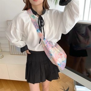 Close-up of floral crossbody bag paired with a ruffled white shirt and pleated black skirt