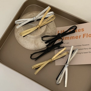 Minimalist leather bow hair clips set in black, gold, and silver on a metal tray