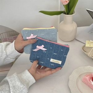 Dettaglio di portamonete in denim con fiocchi rosa e ricami sotto una luce soffusa