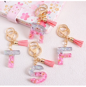 Close-up of pink glitter resin alphabet keychains R T S F with elegant gold tassels