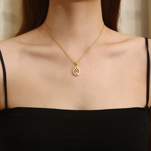 Detail of a gold teardrop necklace with a purple crystal pendant worn by a model