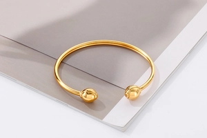 Detailed view of a gold minimalist open bangle featuring spherical ends on a glossy metal surface