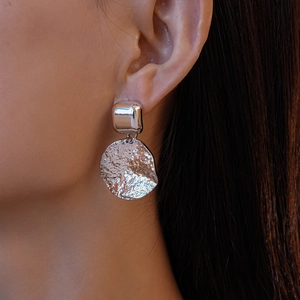 Gros plan de boucles d'oreilles argentées géométriques avec texture martelée sur modèle