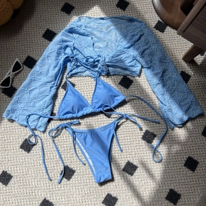 Detailed flat lay of sky blue 3-piece bikini set with textured mesh beach cover-up
