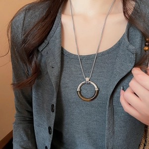 Dettaglio di un ciondolo circolare in resina e metallo argento su un cardigan in maglia grigio