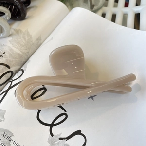 Detail of a cream-colored minimalist hair claw clip with a glossy finish on white paper