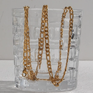 Detail of 5mm gold plated Figaro chain necklace draped inside a textured glass cup