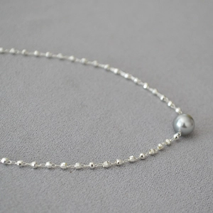 Macro detail of faceted gold beads and a grey pearl on a minimalist brass necklace chain