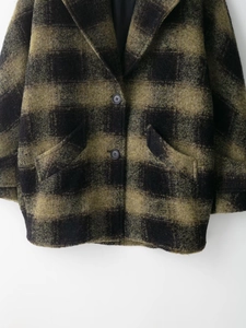 Detail of green and black plaid wool blend coat showing buttons and fabric texture