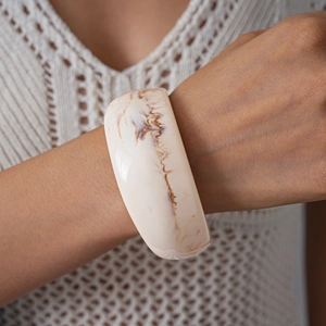 Close-up of a wide marbled acrylic bangle featuring ivory and brown marble textures