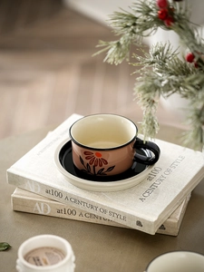 Close-up of pink ceramic coffee cup with hand-painted floral pattern and black saucer