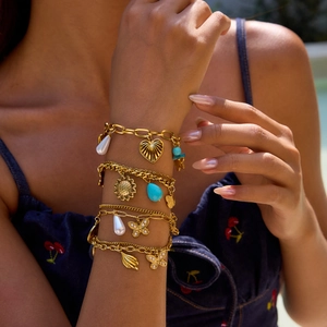 Gros plan de bracelets dorés multicouches avec pendentifs cœur, perle et tournesol au poignet