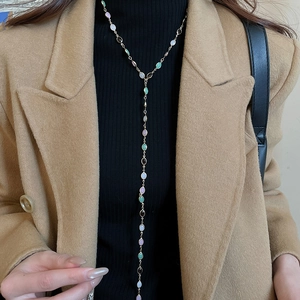 Detailed view of a long Y-shaped gold necklace with colorful oval gems on a model