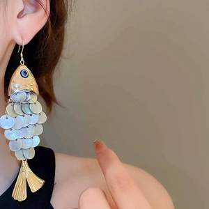 Detail of fish-shaped earrings with pearlescent scales and golden ginkgo leaf pendants