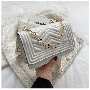 Close-up of white quilted crossbody bag featuring gold floral chain and printed strap