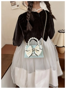 Close-up of a blue houndstooth girl's mini bag with beige bow and pearl handle
