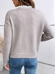 Close-up of elegant white lace collar detail on a loose-fit knitted grey sweater