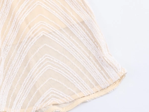 Detailed close-up of wavy white sequins on beige mesh fabric for evening dress