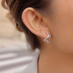 Close-up of dual silver stainless steel crossed lines stud earrings on earlobe