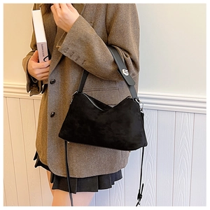 Close-up of black suede crescent shoulder bag with silver buckle on herringbone blazer