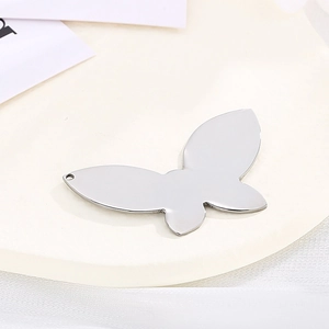Polished stainless steel butterfly pendant on a white tray with minimalist background