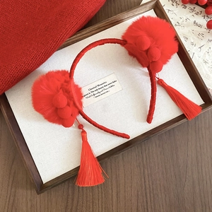Close-up of red festive headband with plush balls and long silk tassels on wood tray