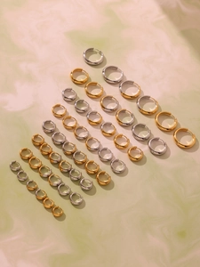 Detail view of mixed size gold and silver stainless steel hoop earrings on marble