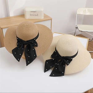 Close-up of wide brim straw hats with black ribbon bows and pearl accents on white table