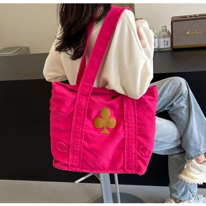 Detail of rose red canvas tote bag with floral patch and fringed edge on model's shoulder