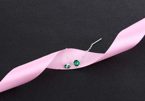 Detail view of S925 silver thread earrings with green zircon on a pink ribbon