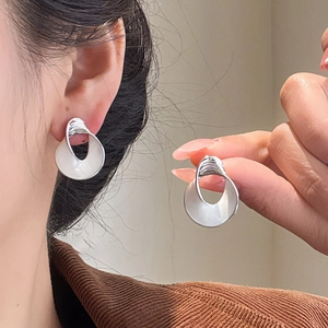 Detail of twisted silver earrings worn by model showing artistic hollow design and gloss