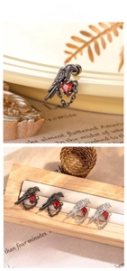 Macro detail of a raven bird stud earring with a red zircon gem and hanging chain
