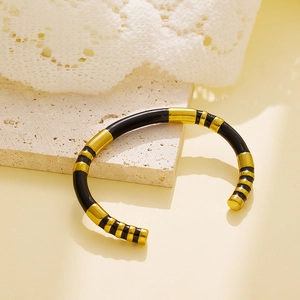 Detail of gold and black enamel segmented cuff bracelet on textured stone surface