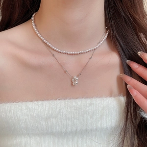 Detail of a double-layer pearl necklace with a flower pendant on a silver-tone chain