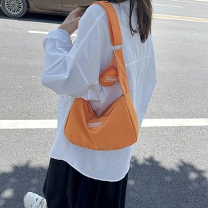 Orange nylon shoulder tote bag with adjustable strap and small round pouch in street view