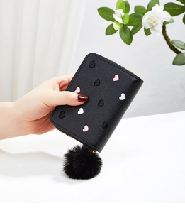 Close-up of black heart-embroidered wallet with a fluffy pom-pom charm on zipper