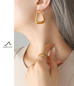 Chic model wearing U-shaped gold earrings and layered rings in 18k plated stainless steel