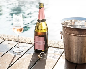 Lifestyle shot of pink champagne bottle with mini stopper by a poolside luxury ice bucket