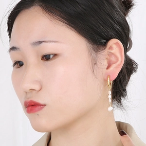 Détail de boucles d'oreilles pendantes dorées avec perles baroques sur un modèle