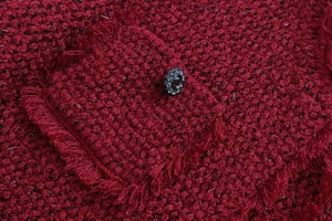 Détail d'une veste en tweed rouge montrant le bord frangé et le bouton décoratif