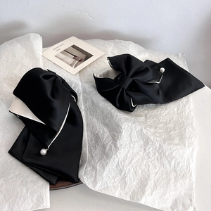 Detail of elegant black fabric bow hair clip with white lining and a pearl center ornament