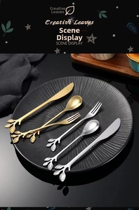 Detail of creative leaf shaped gold and silver stainless steel cutlery set on a black plate