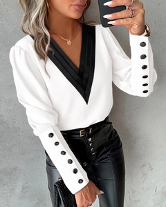 Detail of white V-neck shirt with contrast black trim and multiple buttons on puff sleeves