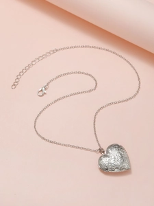 Macro shot of silver heart locket pendant with floral relief on a soft pink background